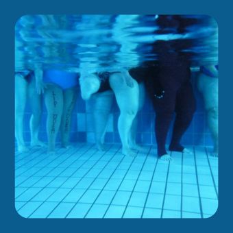 Ein Gruppe steht im Wasser. Zusehen sind nur die Beine. Eine Frau hat auf ihre Beine „Lymphödem“ und „Lipödem“ geschrieben. Das Bild zeigt, dass Betroffene gemeinsam Aquafitness zur Entlastung betreiben.