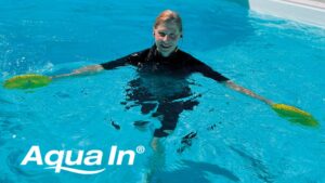 Frau mit schwarzem Neopren-Anzug im Pool. Mit schwarzem Headset und zwei gelben Aqua-Disks in den Händen, im linken unteren Bildausschnitt steht das Aqua In Logo in weißer Schrift.